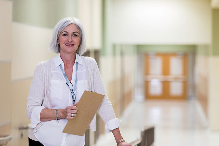 Administrator or staff person standing in school hallway with clipboard in hand